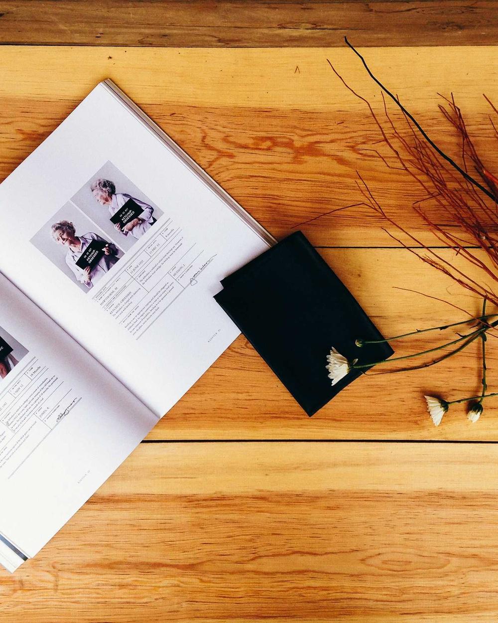 An open magazine, a small black wallet, and dried flowers on a wooden table