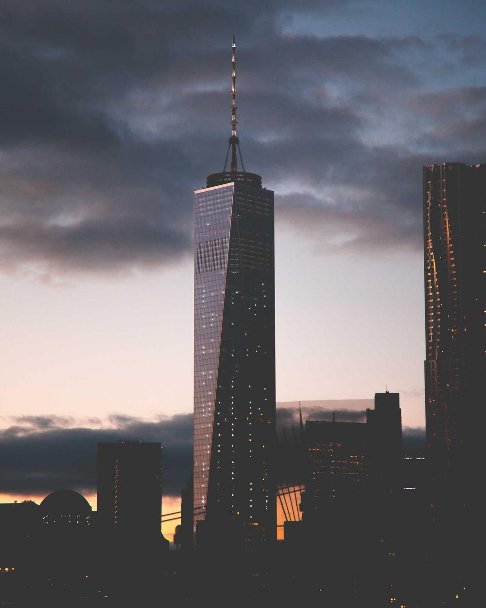 A city skyscraper lit up at dusk beneath dramatic clouds