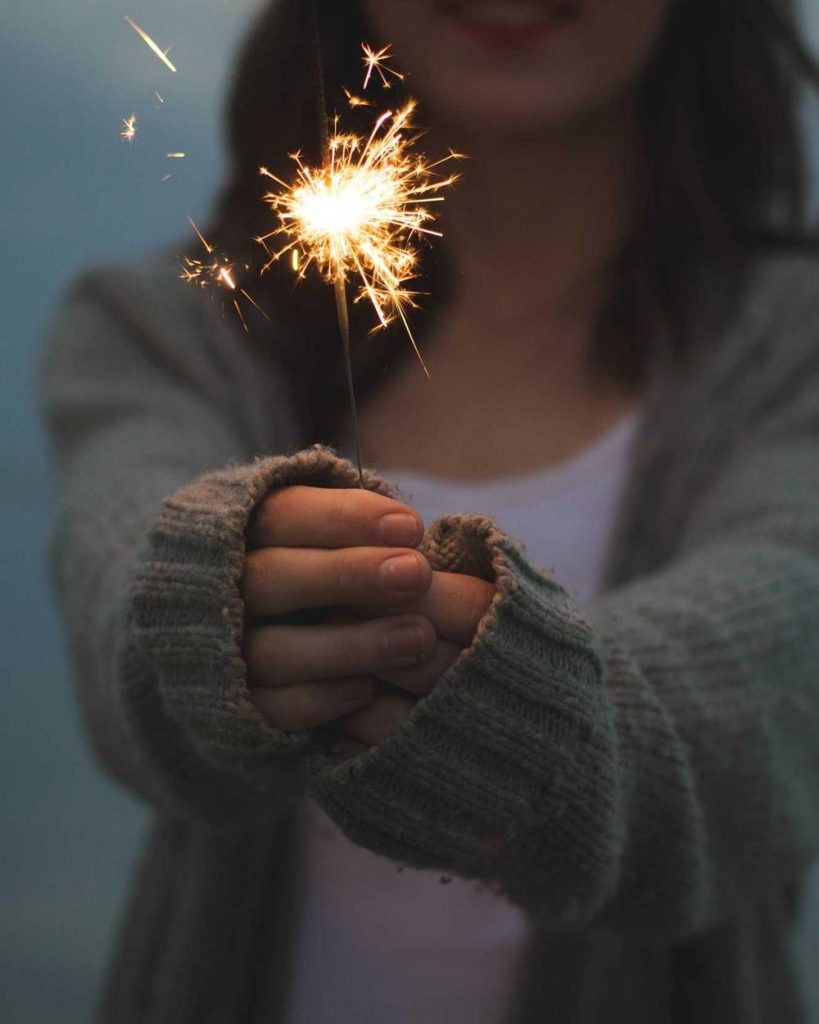 A woman in a cozy cardigan holding a lit sparkler