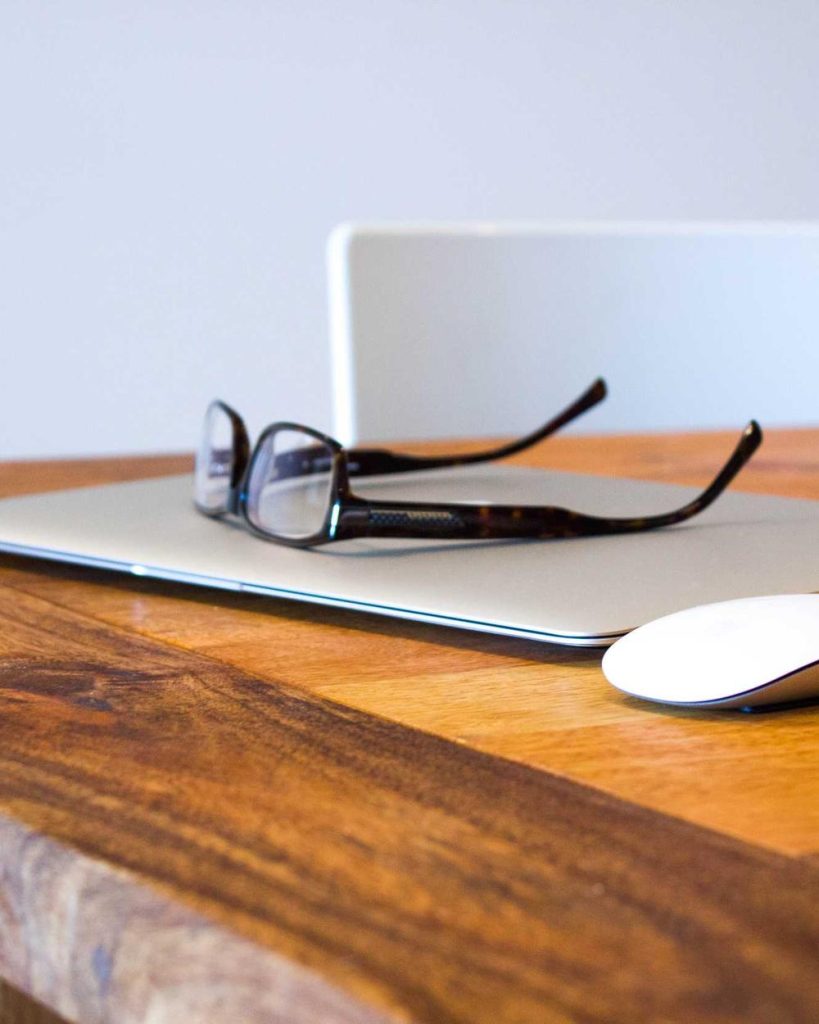 A pair of glasses resting on a closed laptop on a wooden desk