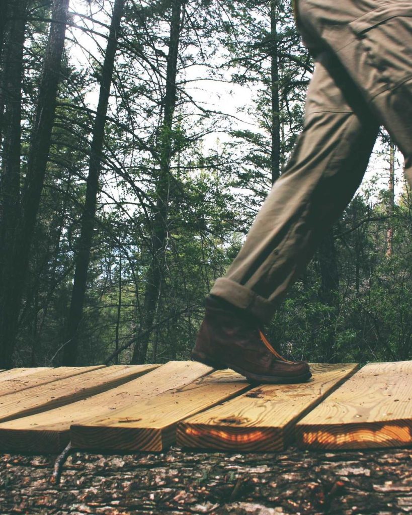 A close-up of a boot stepping onto a wooden boardwalk in a forest